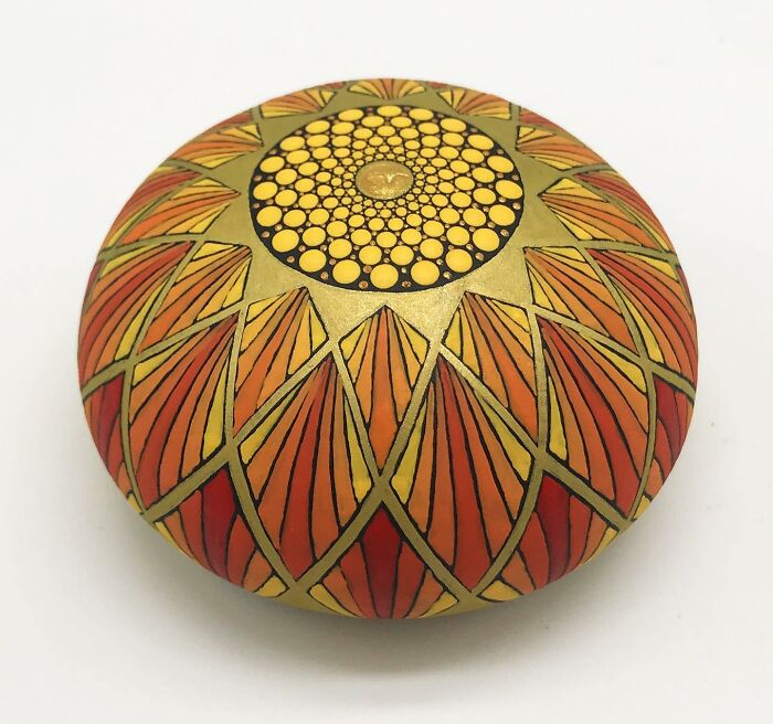 Stone with a beautifully intricate mandala design in orange and yellow hues, showcasing mesmerizing artistry.