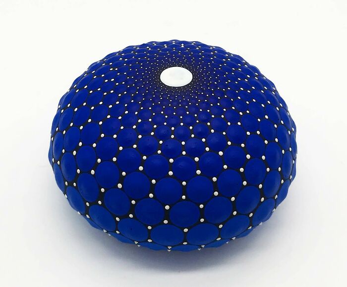 Blue mandala art painted on stone, showcasing intricate dot patterns and a central white dot, embodying mesmerizing beauty.