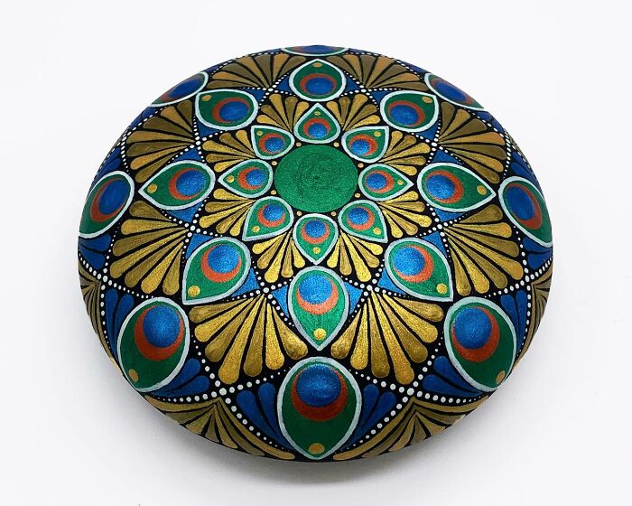 Colorful mandala artwork painted on a stone, featuring intricate patterns in blue, green, and gold tones.