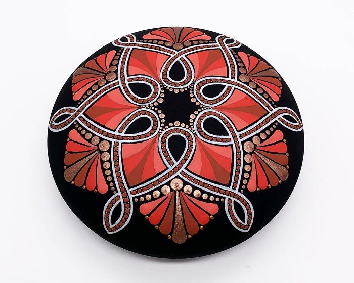 Beautiful mandala art on a stone with intricate red, silver, and bronze patterns.