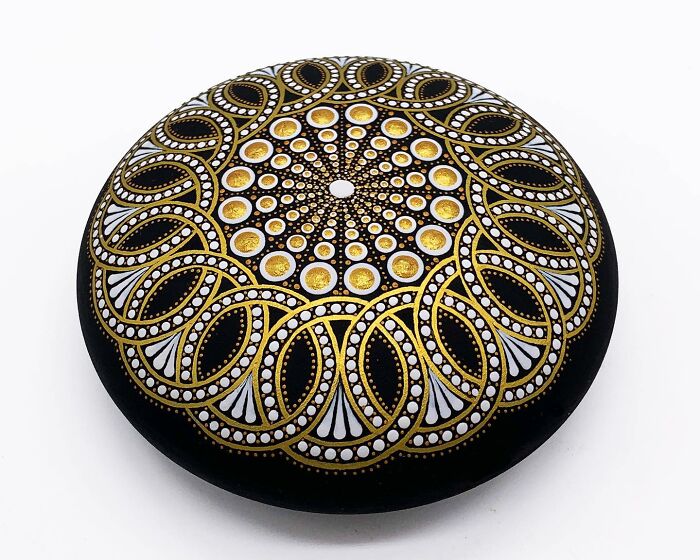 Stone with beautiful mandala art in gold, white, and black patterns.
