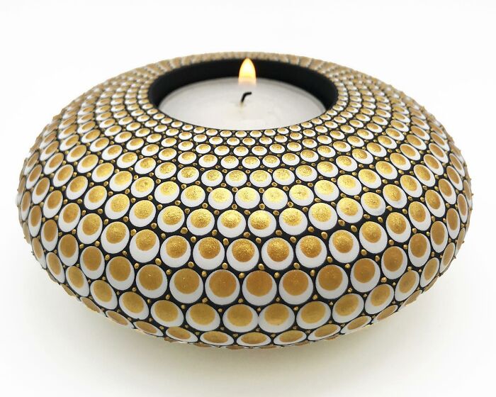 Stone with beautifully painted mandala patterns, featuring intricate gold and white dots, surrounding a lit candle.