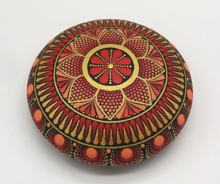 Beautiful mandala artwork painted on a stone, featuring intricate red and gold patterns.