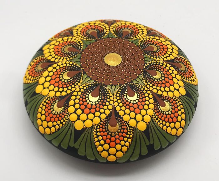 Colorful mandala painted on a stone with intricate, mesmerizing patterns of orange, yellow, and green.