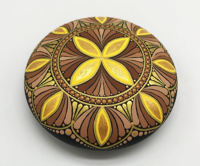 Intricate mandala art painted on a smooth stone, featuring brown and yellow patterns.