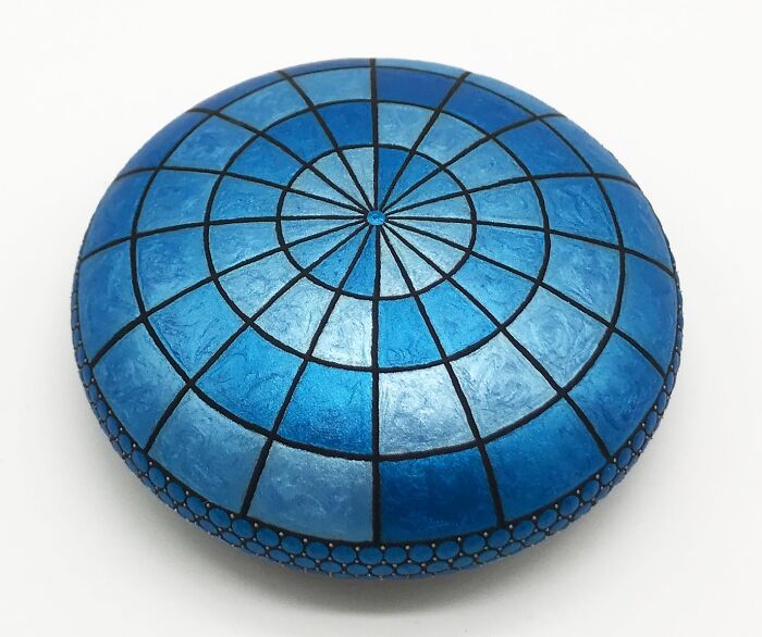 Blue mandala artwork on a stone, featuring intricate geometric patterns and shading.
