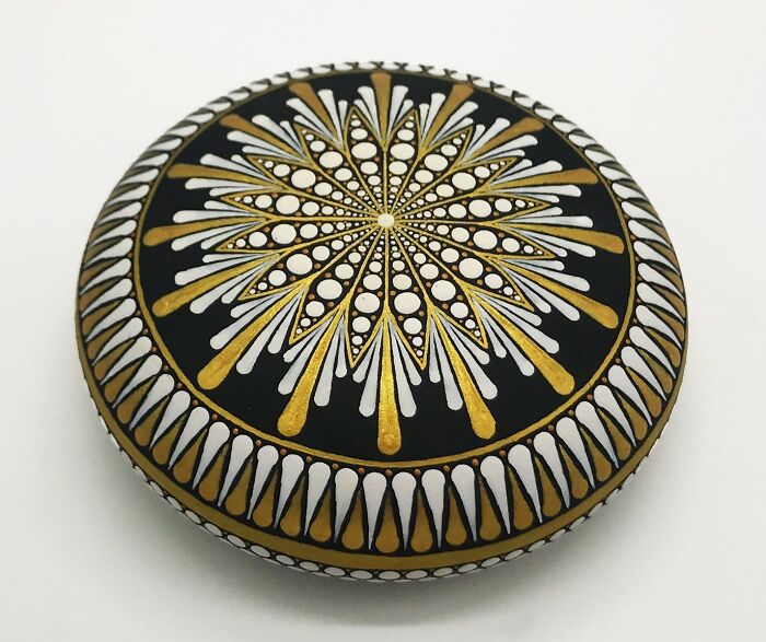 Beautifully painted mandala on a stone with intricate gold and white patterns.