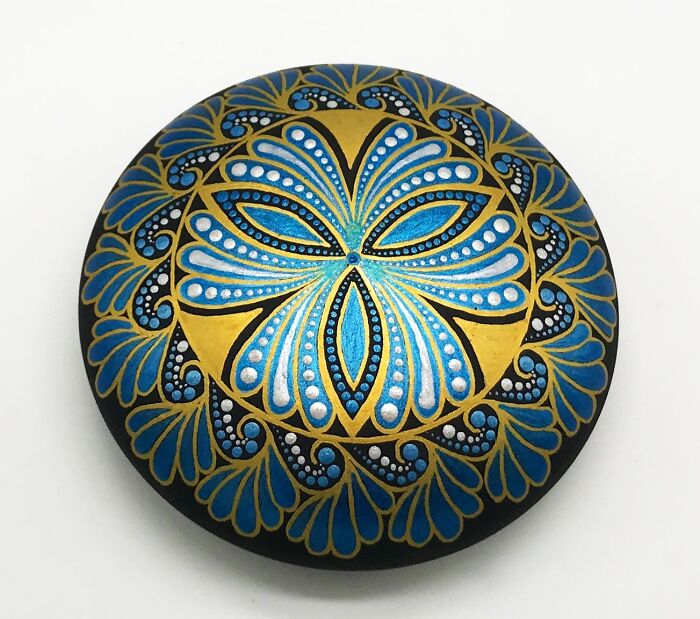 Beautiful mandala art painted on a stone featuring intricate blue and gold patterns.