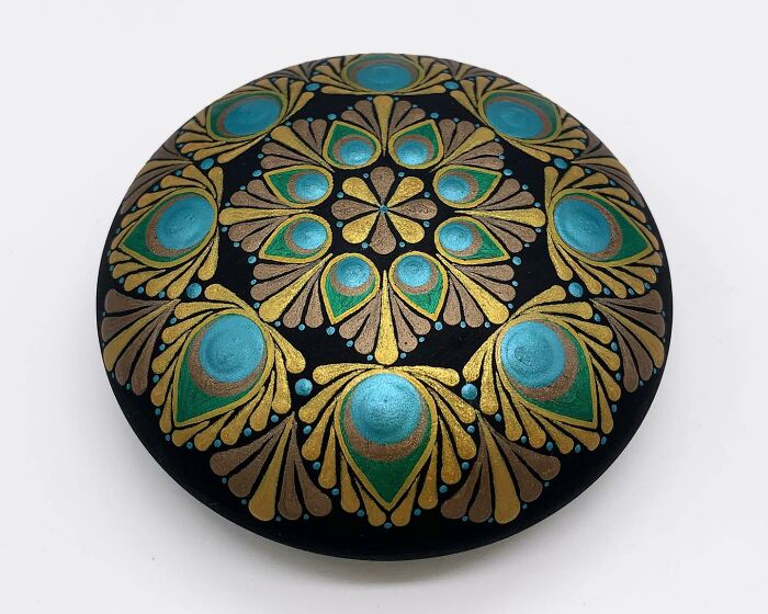 Beautiful mandala painted on a smooth stone with intricate blue and gold patterns.