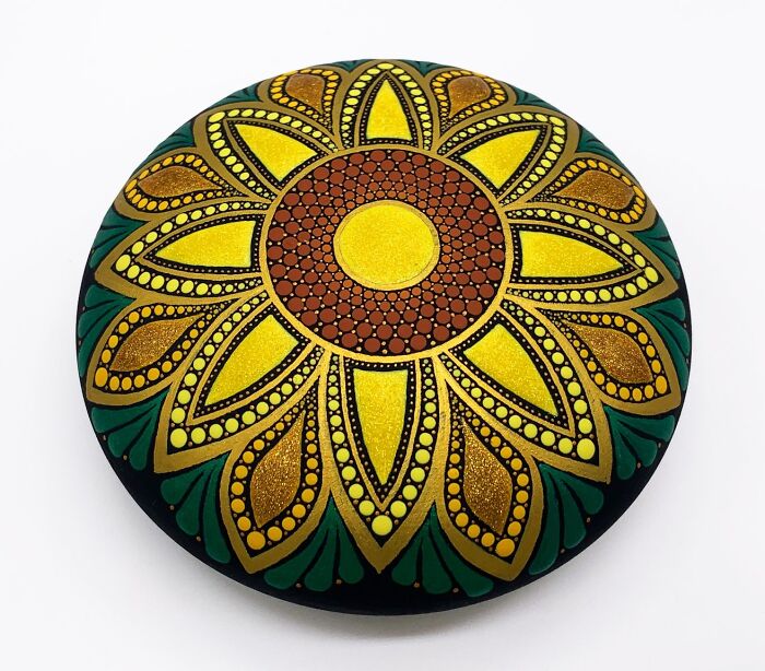 A beautifully painted mandala on a stone with intricate yellow, brown, and green patterns.