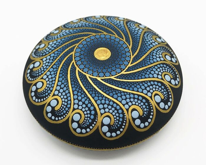 Intricate mandala art on a stone, featuring blue and gold patterns.