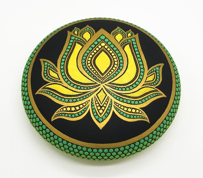 Intricate mandala art painted on a stone, featuring a gold and green lotus design.