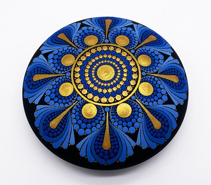 Intricate mandala art featuring blue and gold patterns on a stone.