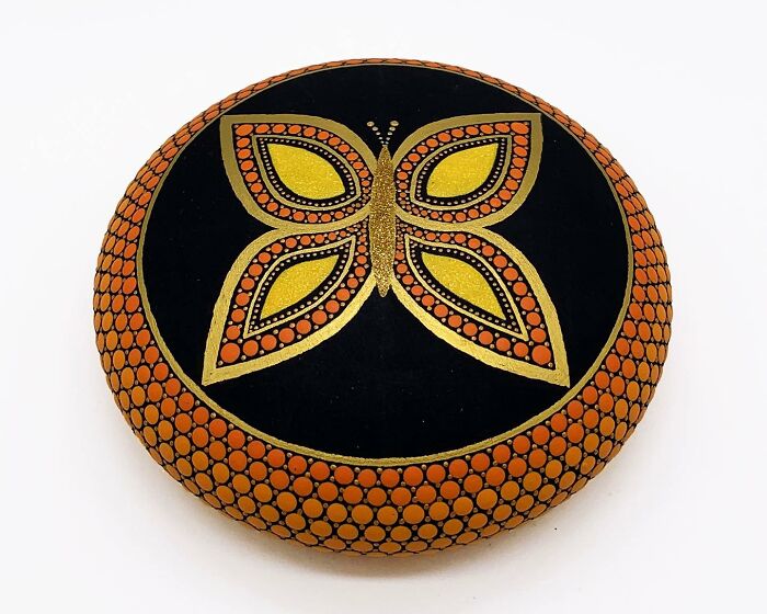 Stone painted with a mesmerizing mandala featuring a butterfly design in orange and gold.