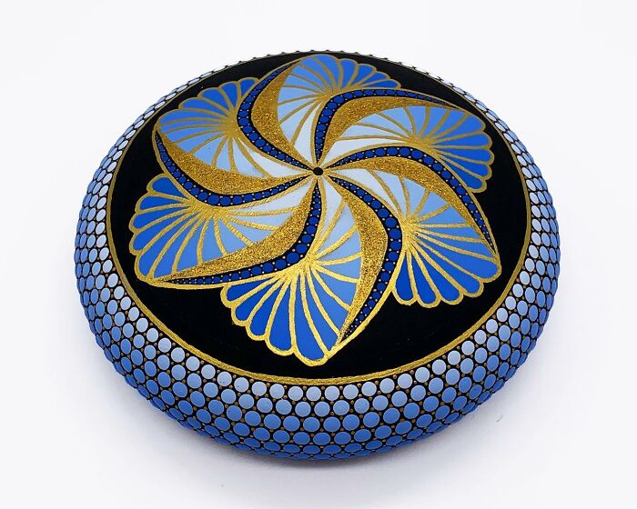 Beautiful mandala art painted on a stone with blue, gold, and black patterns.