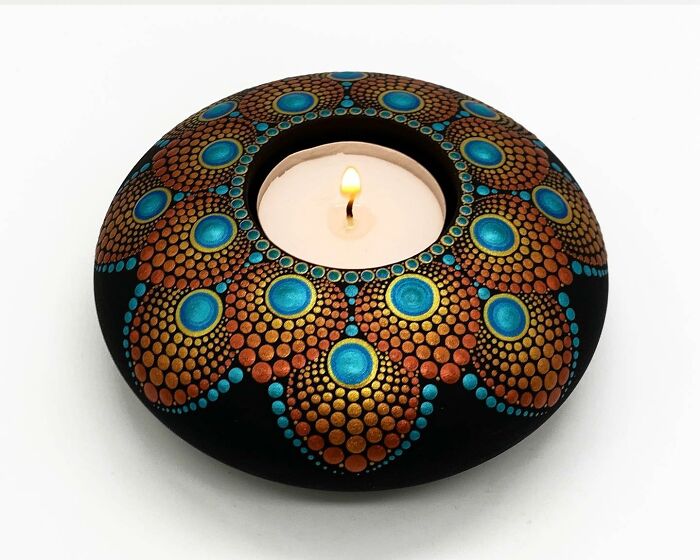 Intricately painted mandala on a stone with a lit candle in the center, showcasing beautiful artistry.
