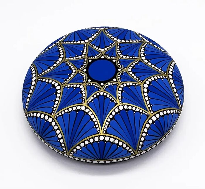 Beautiful mandala art painted on a stone, featuring intricate blue, gold, and white patterns.