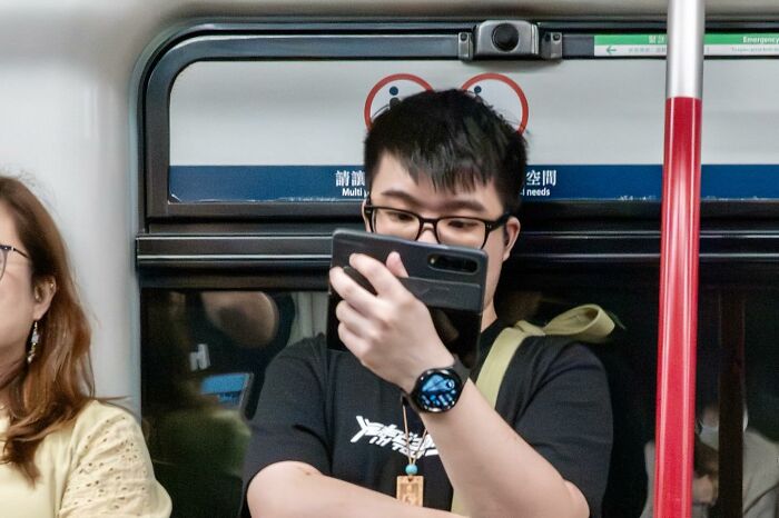 Person on a subway holding a phone, with perfectly timed sign making it look like they have Mickey Mouse ears.