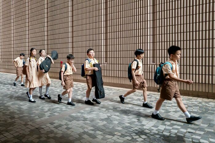 Children in uniform walk in line carrying instruments, showcasing a lucky coincidence in this perfectly timed photo.