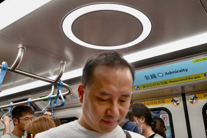 Man perfectly aligned with ceiling light on subway, creating a halo effect.