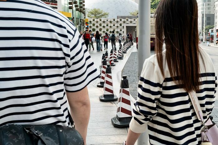 Two people in matching striped shirts walk on a street, creating a lucky coincidence with traffic cones.