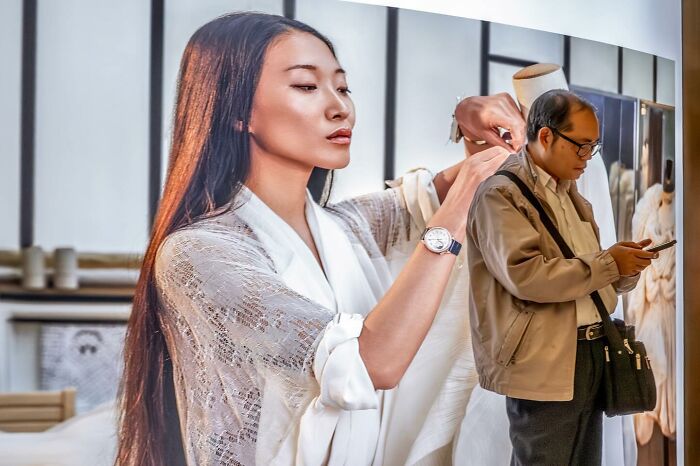 Man using phone perfectly aligned with poster, creating illusion of woman tailoring his jacket; example of lucky coincidences.