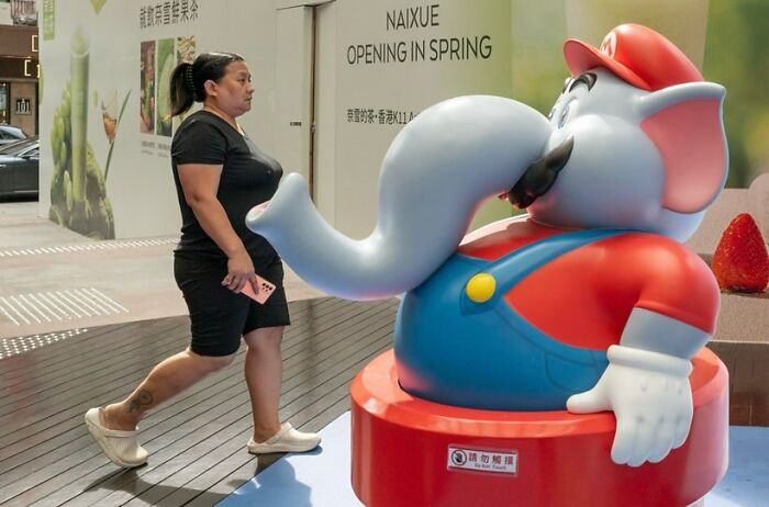 Woman walking past an elephant statue in a perfectly timed picture by Edas Wong.