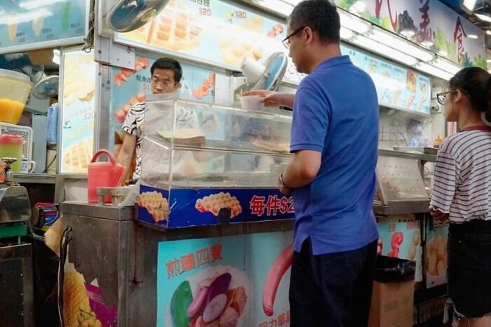 Man in blue shirt at a street food stall, showcasing lucky coincidences with a perfectly timed photo.