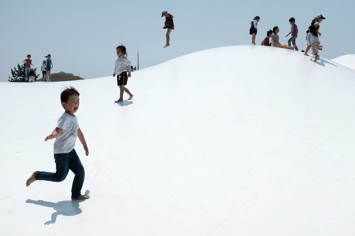 Children playing on a large, white inflatable surface under a clear sky, capturing a perfect coincidence.