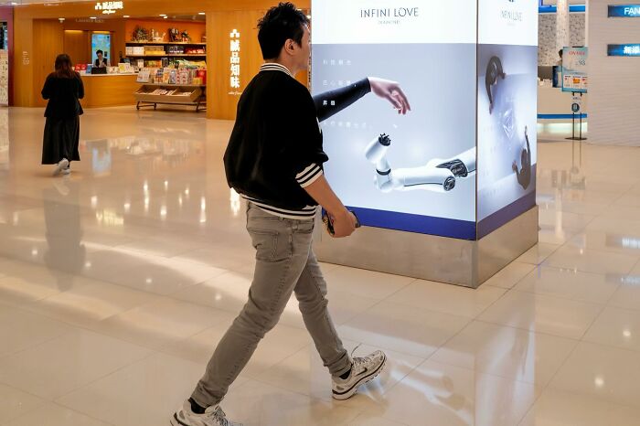 Person walking past an advertisement, creating a perfectly timed optical illusion of a robotic arm as their real arm.