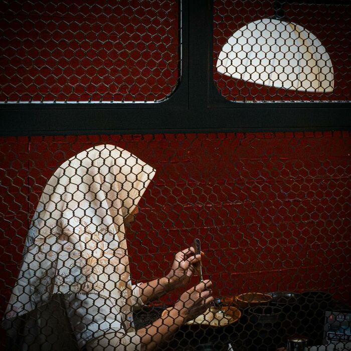 Person dining behind a mesh screen, with light forming a halo effect, showcasing a perfectly timed picture by Edas Wong.