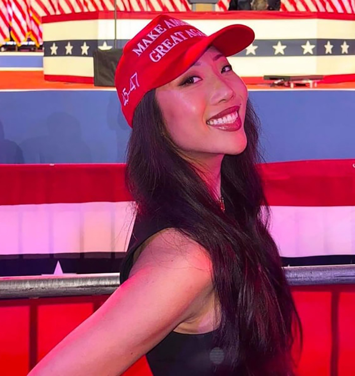 Right-wing influencer in a red MAGA hat at a political event, smiling and facing the camera.