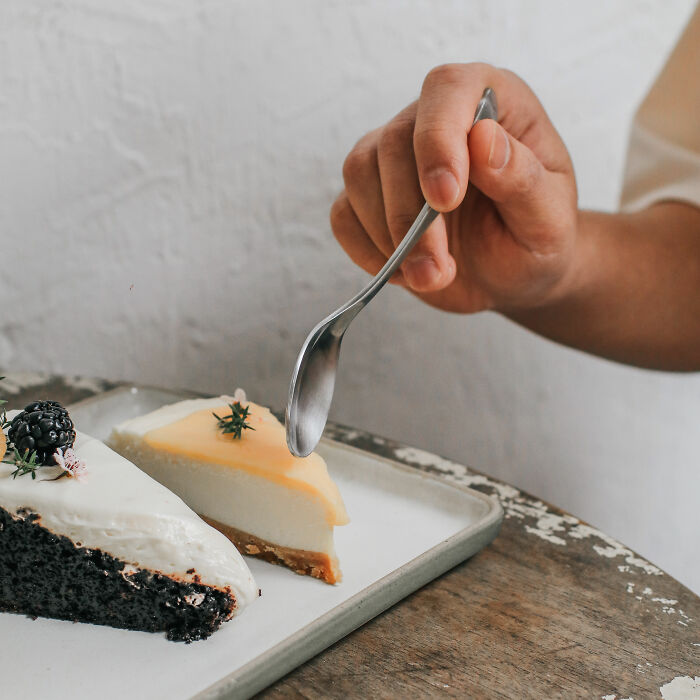 Hand holding a fork near slices of cheesecake, highlighting European dessert presentation.