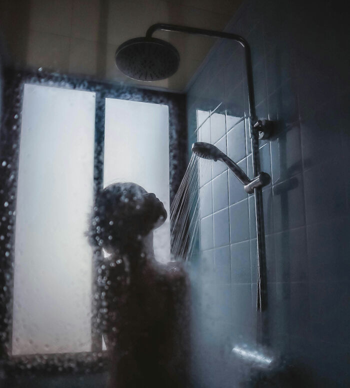 Person showering in a European-style bathroom with frosted glass window, capturing a moment of daily life.