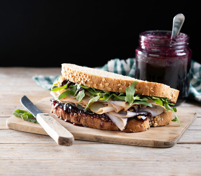 Sandwich with turkey and arugula on a cutting board, next to a jar of jam, highlighting Americans' thoughts on Europe.