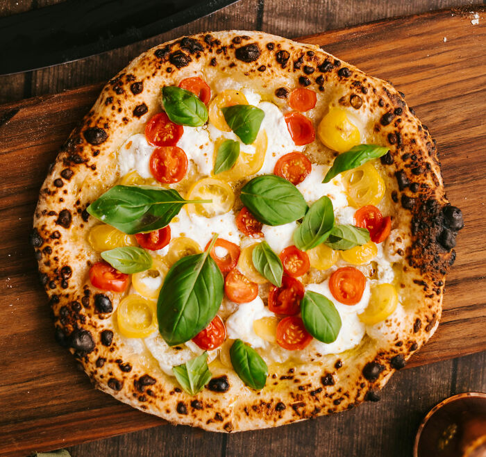 European-style pizza with colorful cherry tomatoes and fresh basil leaves on a wooden board.