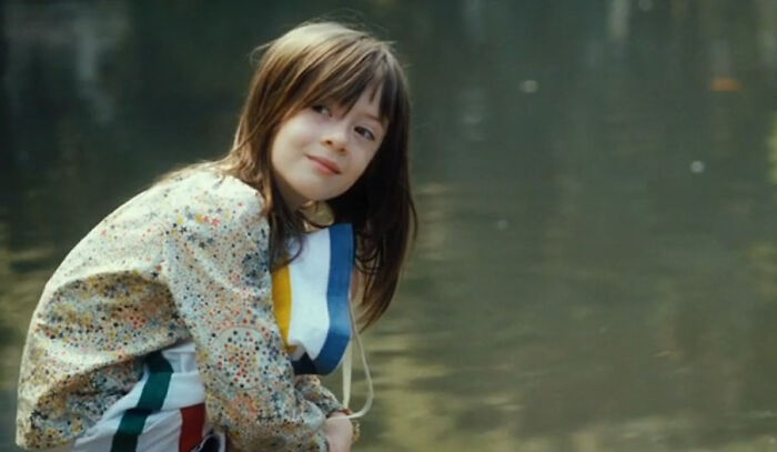 Young girl in a floral shirt by the water, evoking emotions tied to movies that cause tears.