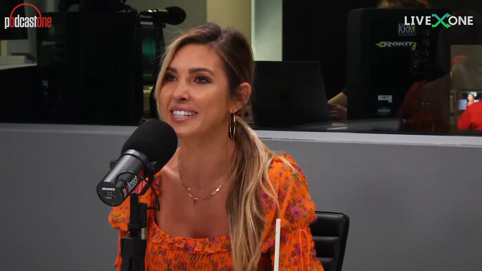 Woman wearing an orange floral top speaking into a microphone during a podcast about celebrity home break-ins.