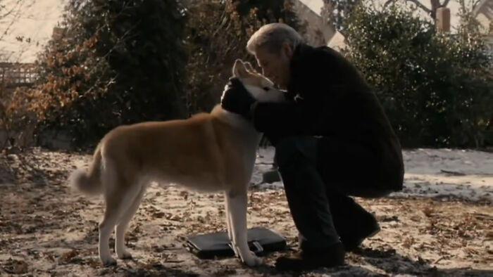 Man kneeling, embracing a dog outdoors on a snowy ground.