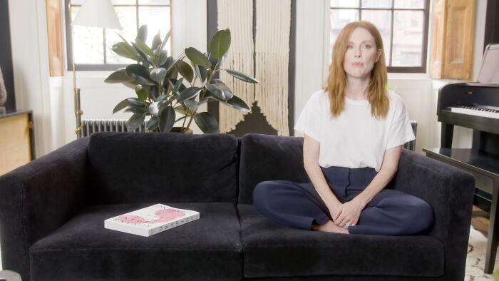 Woman sitting cross-legged on a black couch in a bright room with plants and a piano, discussing celebrity home break-ins.