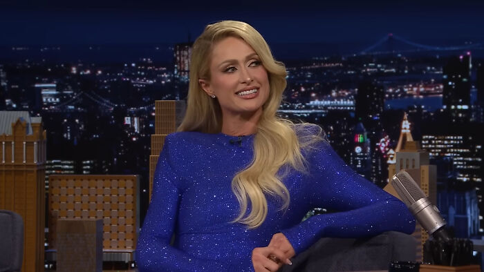 Blonde woman in a sparkling blue dress sitting on a late night talk show set discussing celebrity homes break-ins.