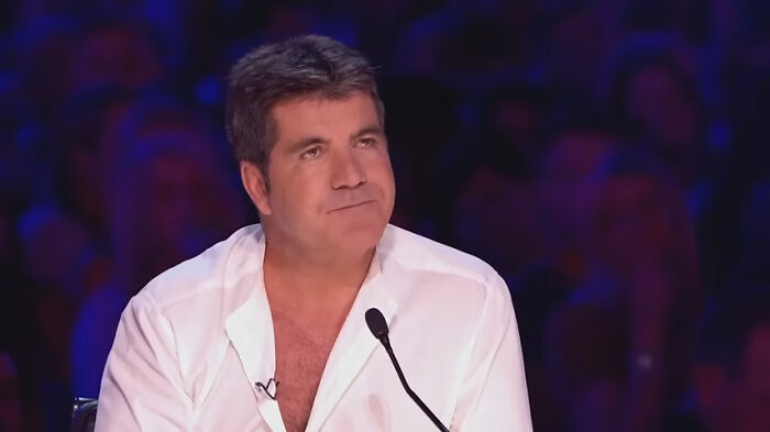 Man in a white shirt sitting at a microphone during a talent show, related to celebrity homes break-in incidents.