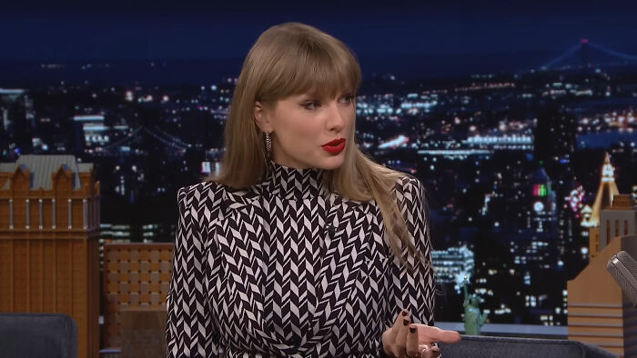 Taylor Swift speaking on a nighttime talk show set, discussing her experiences with celebrity homes being broken into.