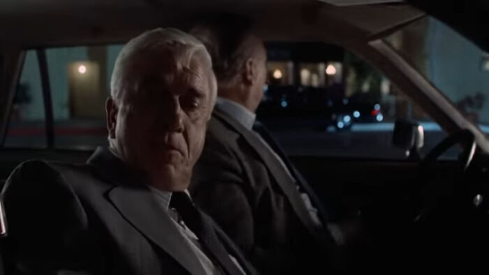 Two men in suits sitting in a car at night, illustrating things that look awesome in movies but are terrible in real life.