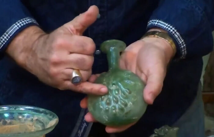 Hands examining an ancient artifact, a green glass bottle, with intricate details that intrigue scientists.