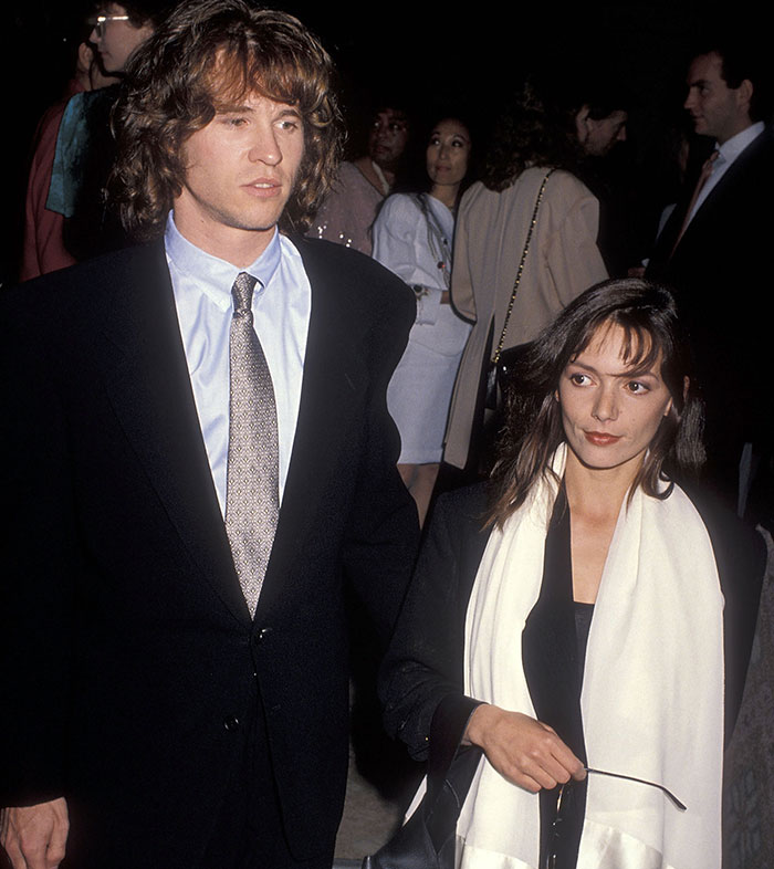A man in a suit and a woman with a scarf at a formal event, amid a lively Hollywood gathering.