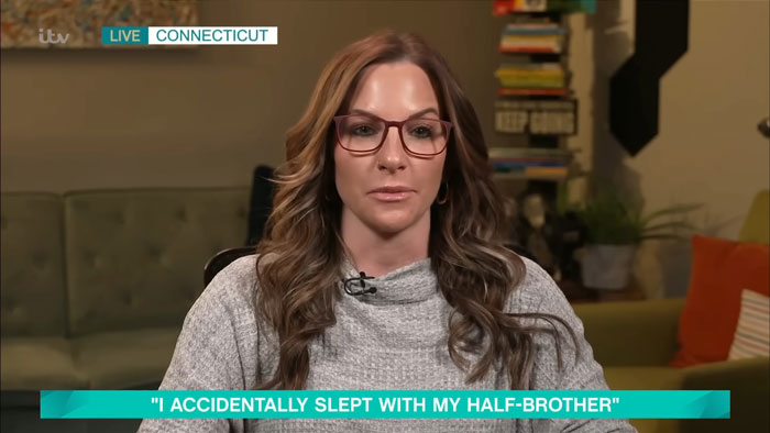 Woman discussing fertility fraud, wearing glasses and a gray sweater, in a live TV interview setting.