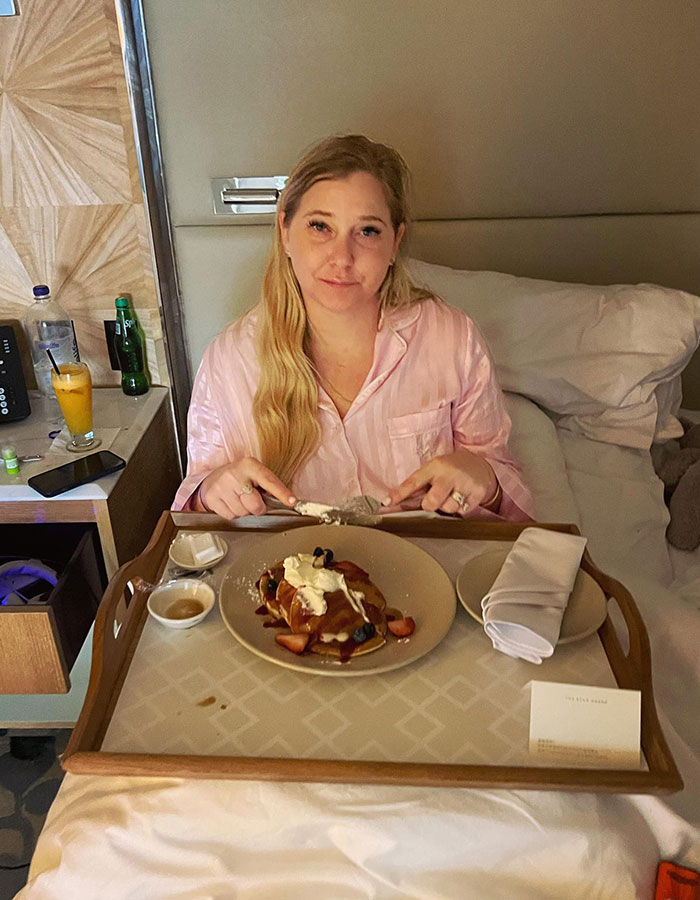 Woman in pink pajamas having breakfast in bed with pancakes; Prince Andrew's ex criticized for social media post.