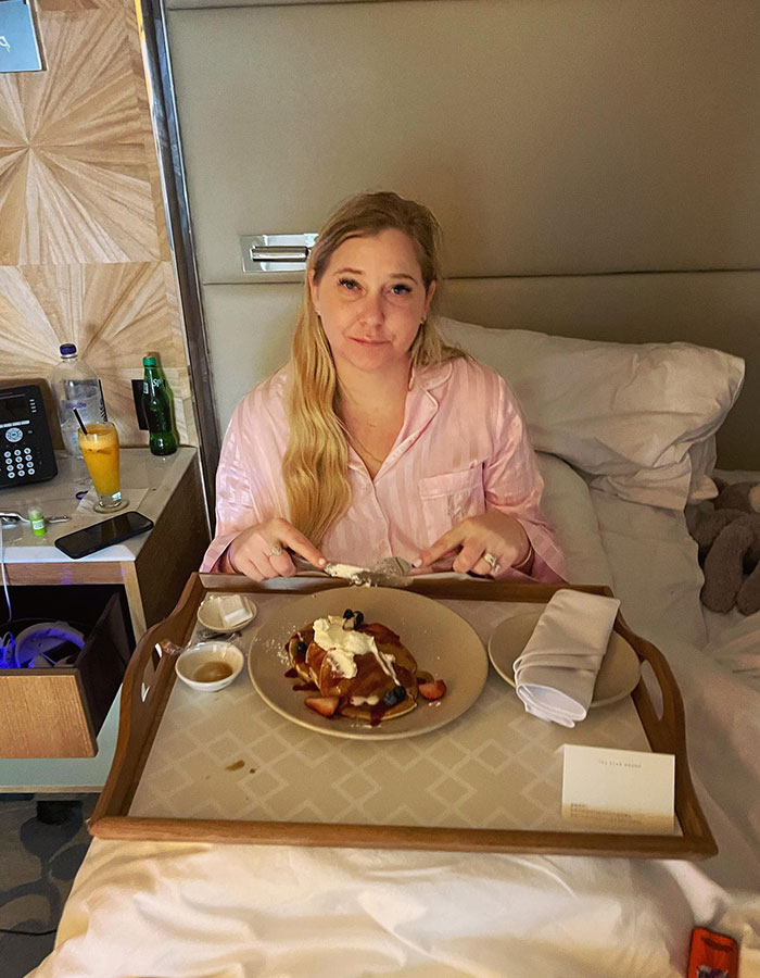 Woman in pink pajamas with breakfast tray in bed, linked to Virginia Giuffre's chilling post and passing theories.