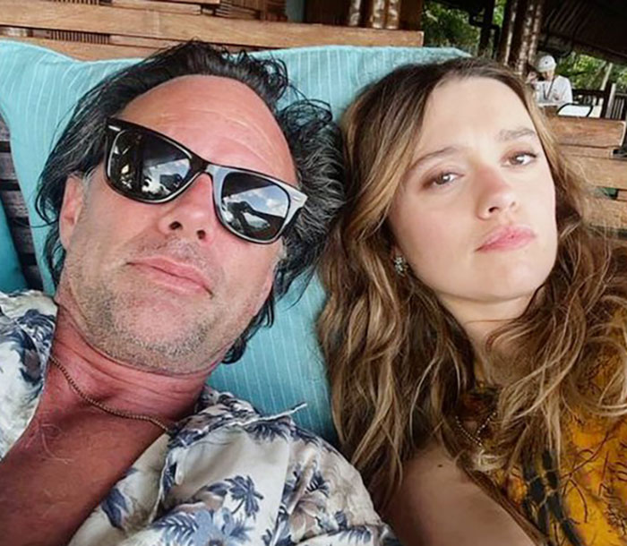 A man in sunglasses and a floral shirt with a woman, both relaxing on a lounge chair outdoors.